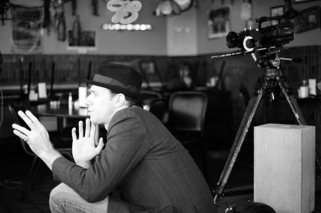 Man with hat gestures near camera in black and white photo