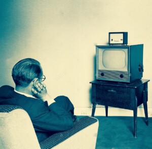 historical 1950s picture shows man sitting in-an armchair watching TV