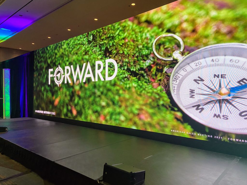 led wall showing the word Forward and time piece on a lush green background