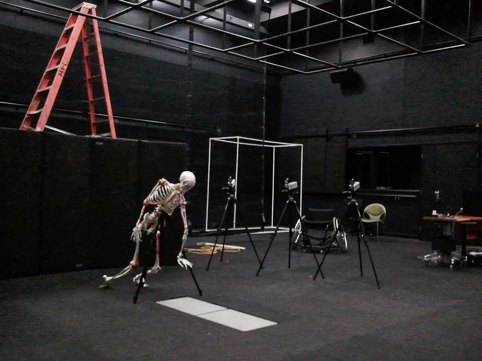A skeleton hangs in a open room with cameras arranged for a photo shoot.